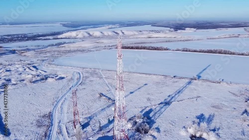 Winter. Telephone communication tower. TV repeater. Drone shooting. Blue sky. Sunny day. The tower is red and white. Tall construction, metal structure.