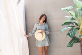 Beautiful woman in summer dress and straw hat by palm tree and gray wall on background, playful joyful  positive excited cheerful happy