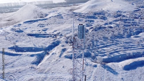Winter. Telephone communication tower. TV repeater. Drone shooting. Blue sky. Sunny day. The tower is red and white. Tall construction, metal structure.