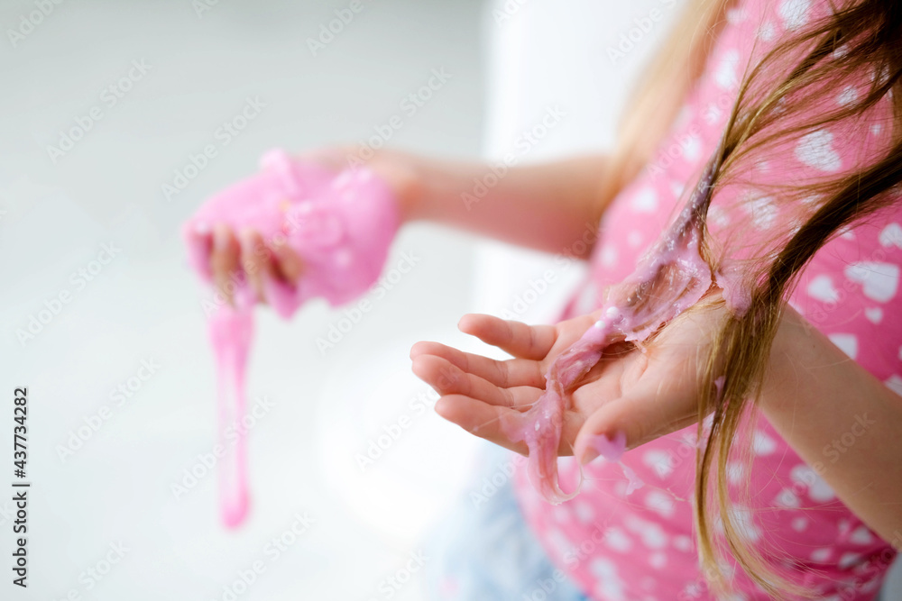 Naklejka premium A little girl stained her hair with slime. Child hair tangled in pink slime.