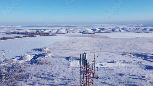 Winter. Telephone communication tower. TV repeater. Drone shooting. Blue sky. Sunny day. The tower is red and white. Tall construction, metal structure.