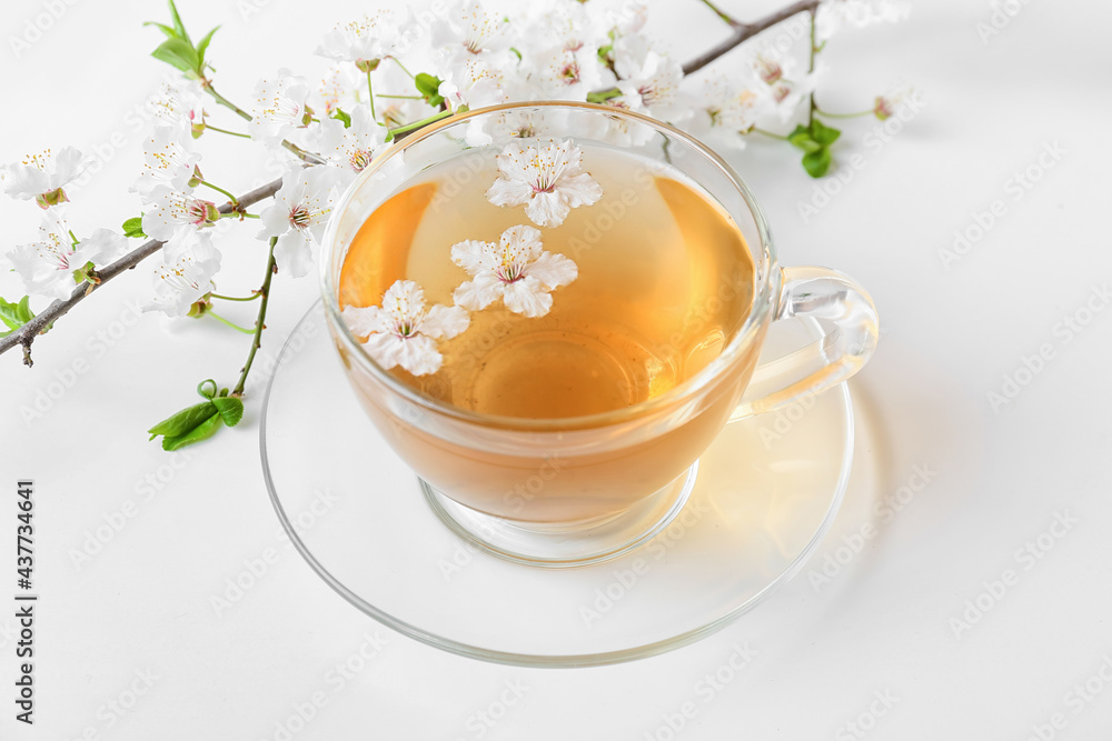 Cup with tasty tea and blooming branches on light background Cup with tasty tea and blooming branches on light background