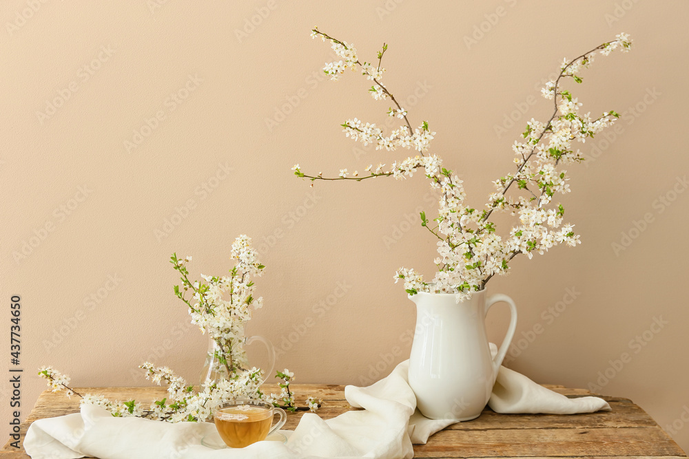 Cup with tasty tea and jug with blooming branches on wooden table Cup with tasty tea and jug with blooming branches on wooden table