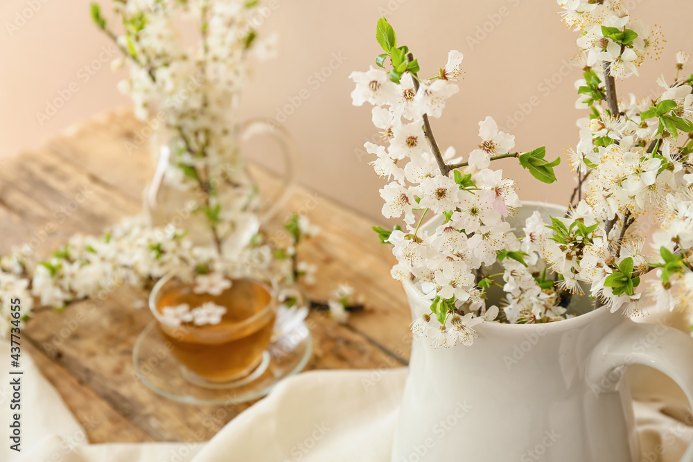 Cup of tasty tea and vase with blooming branches on wooden table