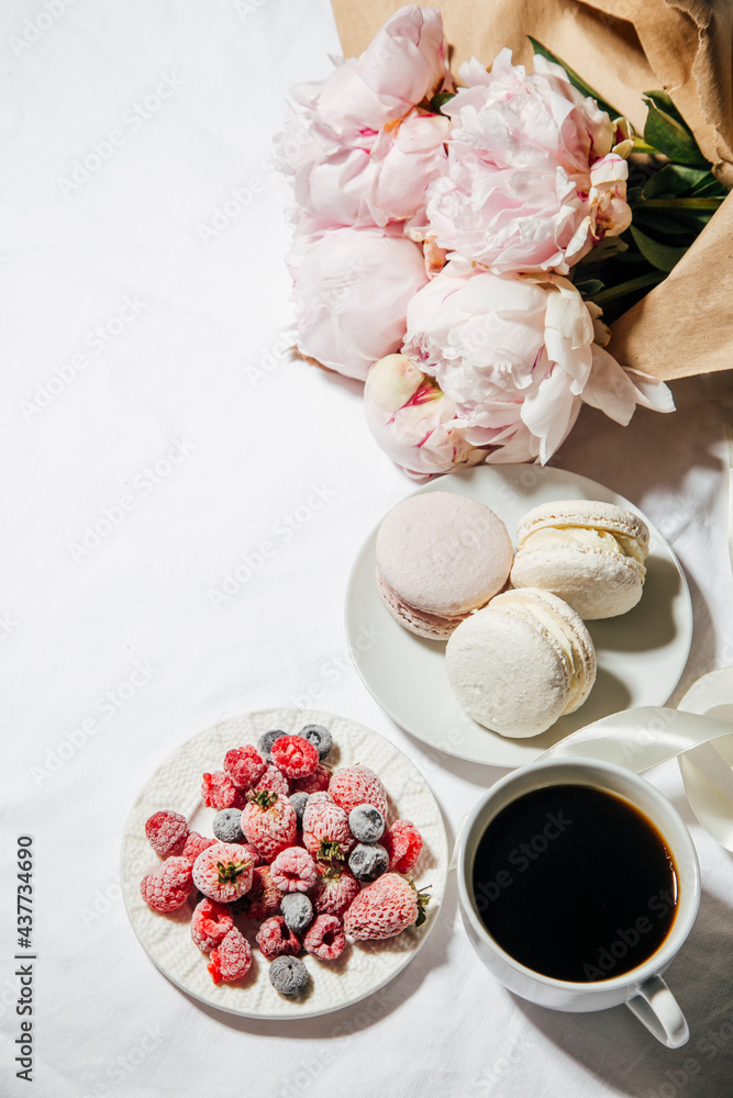 coffee, peonies and macaroons on white bed linen. Breakfast in bed. Scandinavian style. Flat lay, top view coffee, peonies and macaroons on white bed linen. Breakfast in bed. Scandinavian style. Flat lay, top view