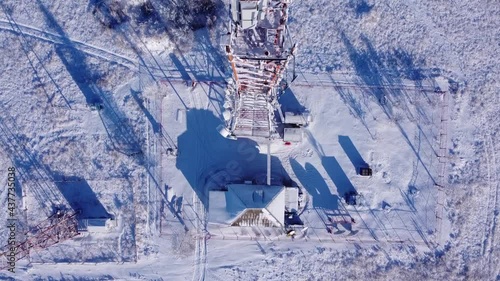 Winter. Telephone communication tower. TV repeater. Drone shooting. Blue sky. Sunny day. The tower is red and white. Tall construction, metal structure.