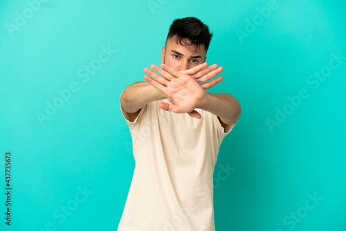 Young caucasian man isolated on blue background making stop gesture with her hand to stop an act