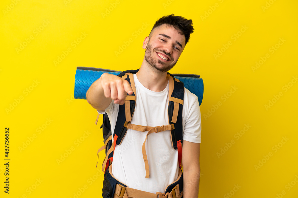 Young mountaineer caucasian man with a big backpack isolated on yellow background pointing front with happy expression Young mountaineer caucasian man with a big backpack isolated on yellow background pointing front with happy expression