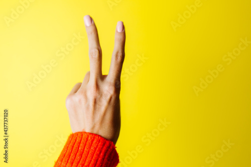 Woman's hand in red sweater shows V piece gesture on yellow background