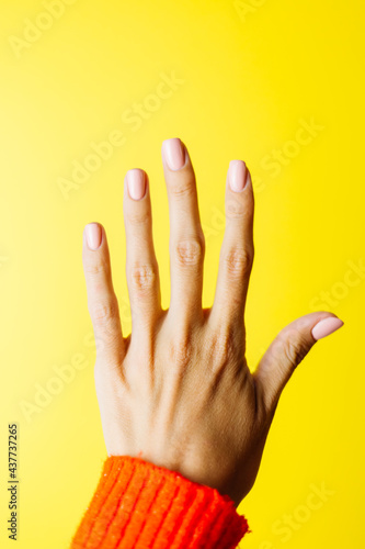 Woman's hand in red sweater shows five with fingers on yellow background