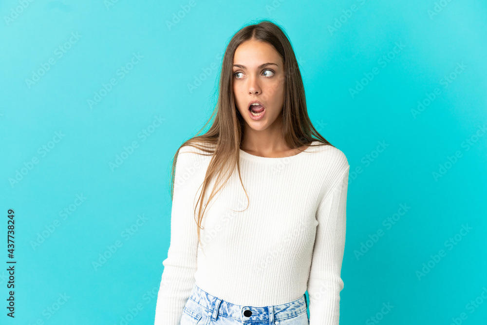 Young woman over isolated blue background doing surprise gesture while looking to the side Young woman over isolated blue background doing surprise gesture while looking to the side