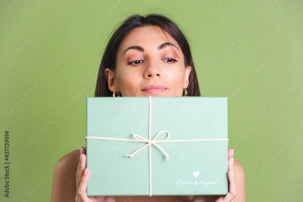 Woman in silk golden dress on green background holding gift box happy positive excited cheerful posing Woman in silk golden dress on green background holding gift box happy positive excited cheerful posing