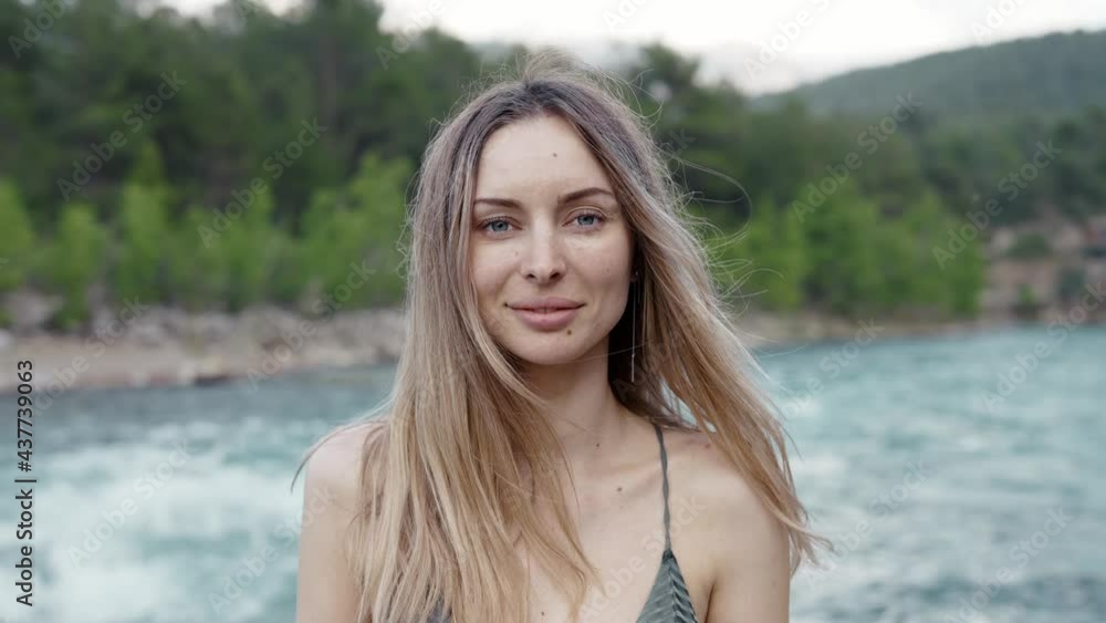 Carefree woman standing in front camera - green hills and river on background Carefree woman standing in front camera - green hills and river on background