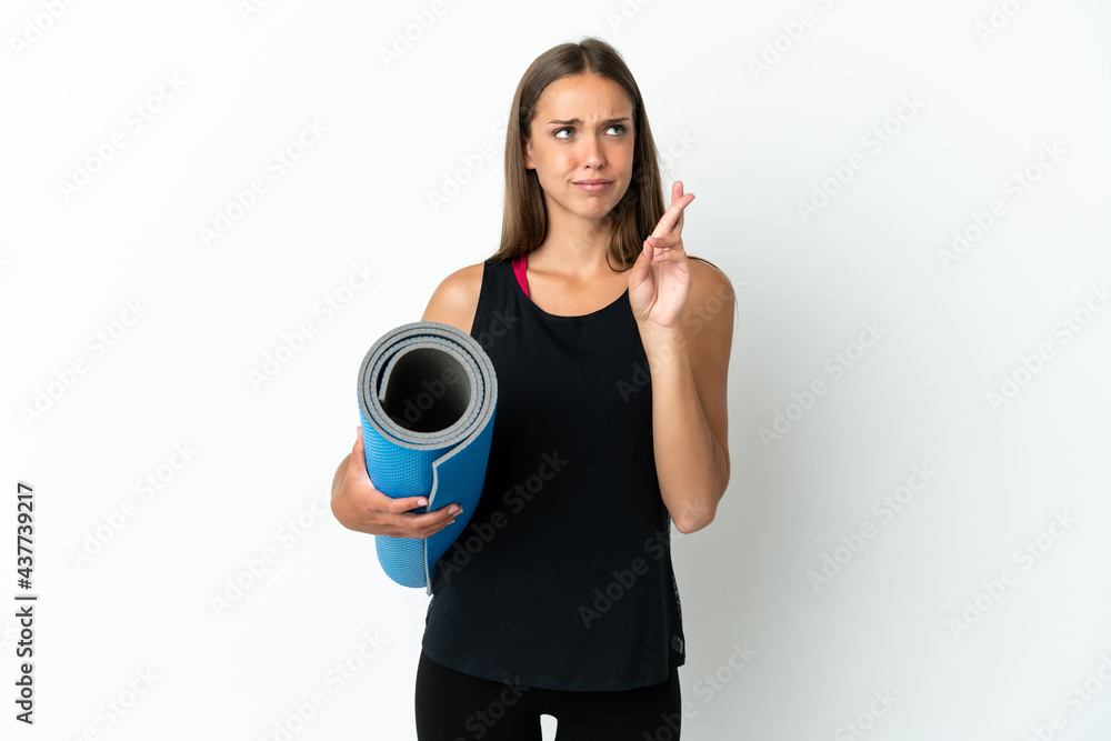Sport woman going to yoga classes while holding a mat over isolated white background with fingers crossing and wishing the best Sport woman going to yoga classes while holding a mat over isolated white background with fingers crossing and wishing the best