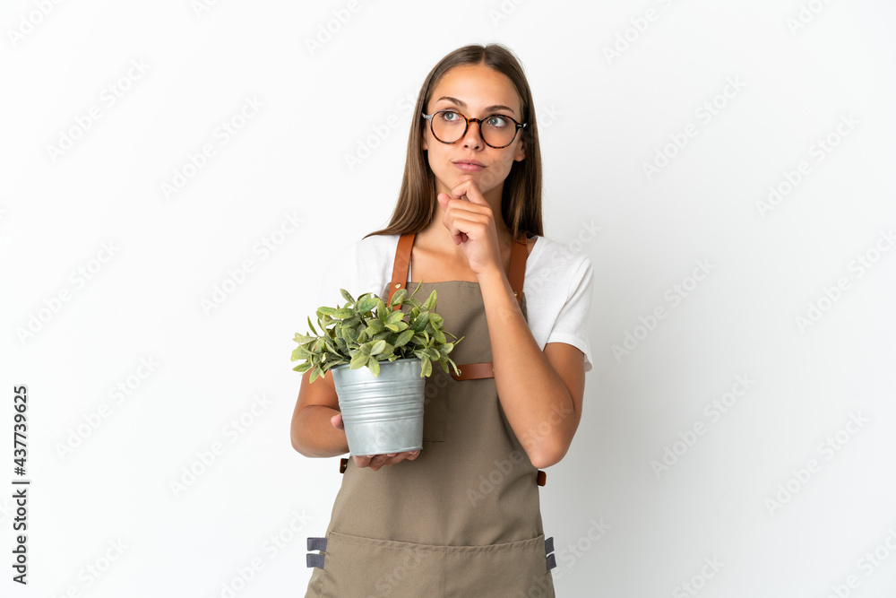 Gardener girl holding a plant over isolated white background and looking up Gardener girl holding a plant over isolated white background and looking up