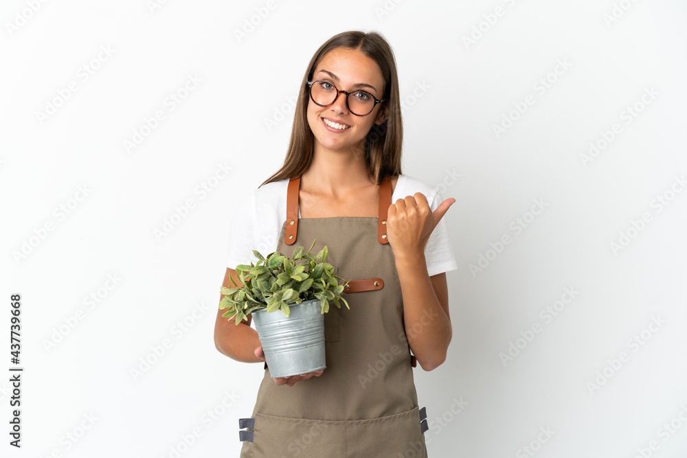 Gardener girl holding a plant over isolated white background pointing to the side to present a product Gardener girl holding a plant over isolated white background pointing to the side to present a product