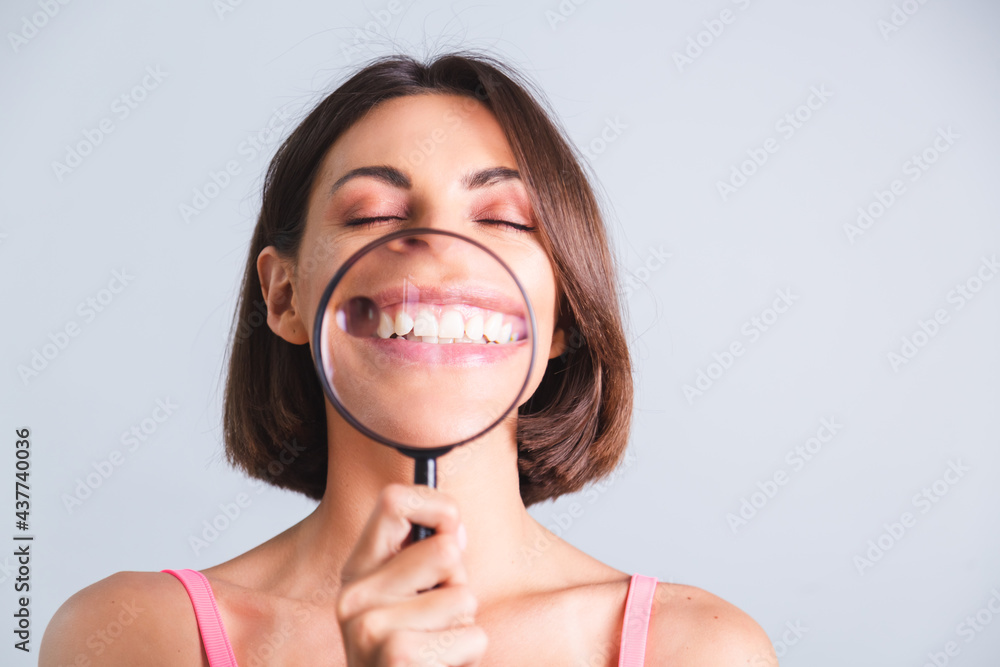 Pretty woman on gray background held magnifier happy showing white snow teeth smile Pretty woman on gray background held magnifier happy showing white snow teeth smile