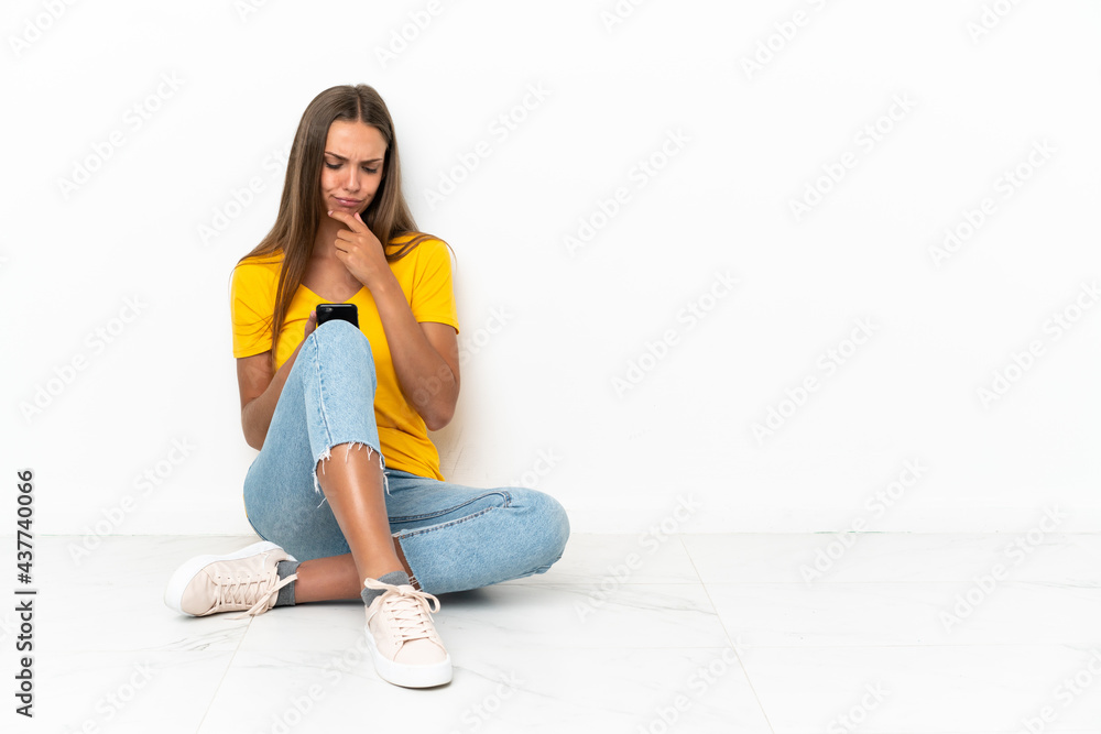 Fototapeta premium Young girl sitting on the floor thinking and sending a message