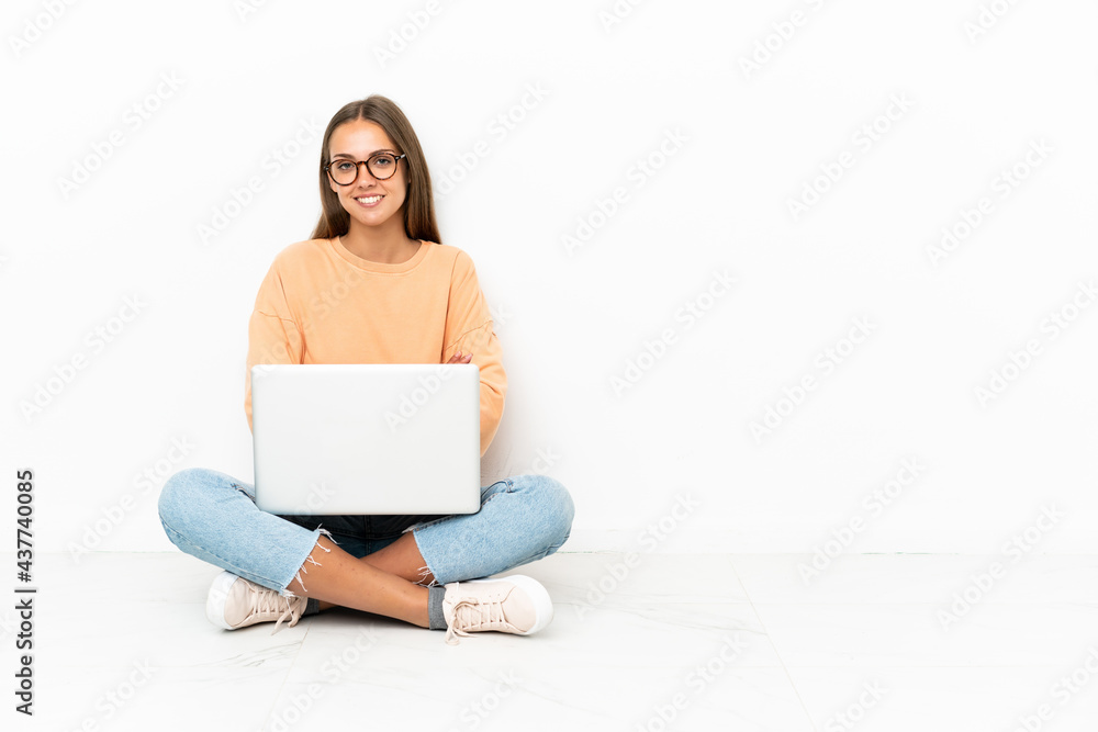 Naklejka premium Young woman with a laptop sitting on the floor keeping the arms crossed in frontal position