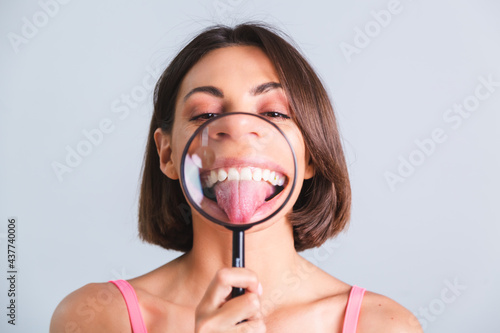 Pretty woman on gray background held magnifier happy shows her tongue