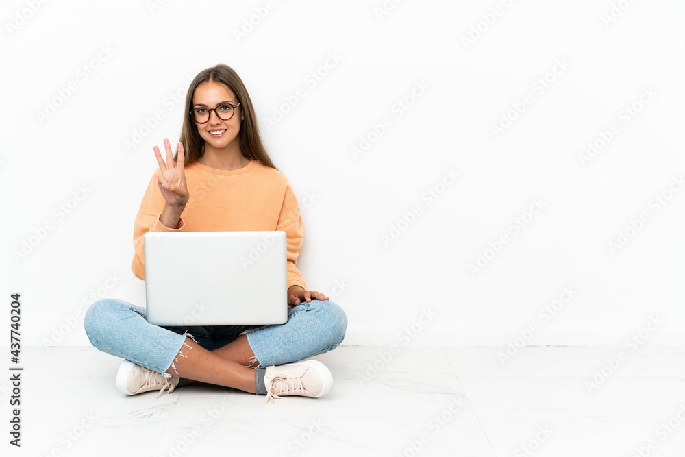 Young woman with a laptop sitting on the floor happy and counting three with fingers Young woman with a laptop sitting on the floor happy and counting three with fingers