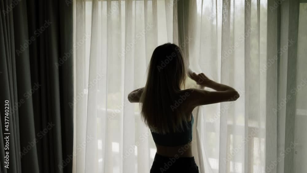 Woman opens curtains, enjoying wellbeing, light and green colors in the morning Woman opens curtains, enjoying wellbeing, light and green colors in the morning
