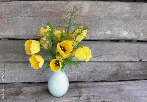 Yellow tulips are a symbol of the sun, smiles and happiness .A large bouquet of bright yellow tulips with green leaves in a white vase. The background is rough old boards. Place for an inscription.