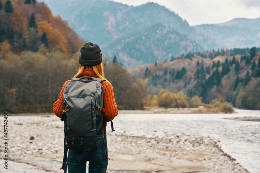 woman travels in the mountains in autumn near the river in nature with a backpack back view