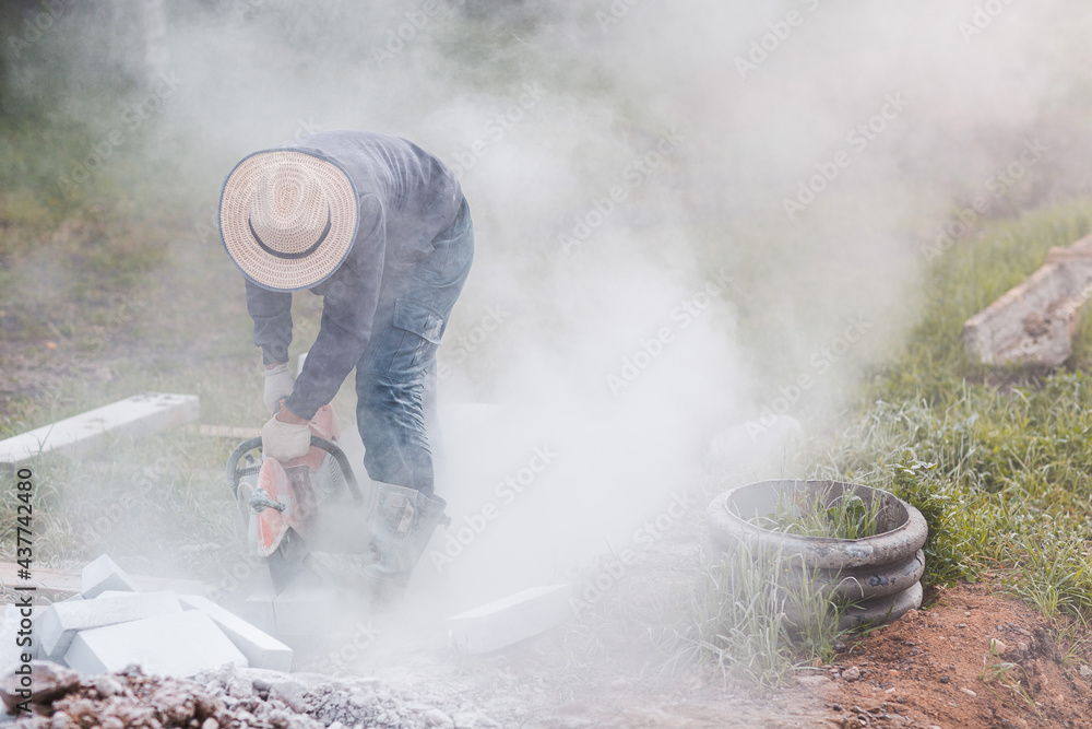 Fototapeta premium Worker mason cuts the sidewalk tile with circular saw while repairing sidewalk in city street.