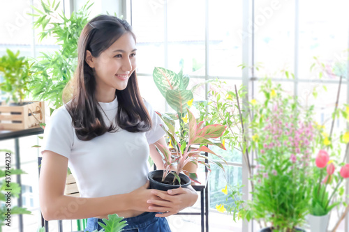 Portrait of Young smiling woman gardening in glasses wearing overalls, taking care for orchid, Home gardening, love of houseplants, freelance, Attractive cute woman gardener smelling in greenhouse © Montri