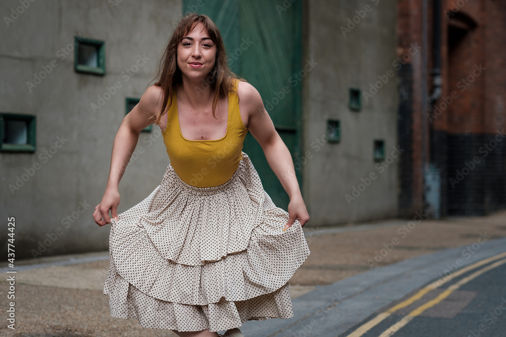Young woman in a yellow t shirt and white skirt posing in a narrow