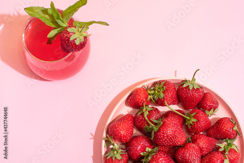 Plate with ripe strawberries and glass of strawberry lemonade on pink background, top view, summer concept.