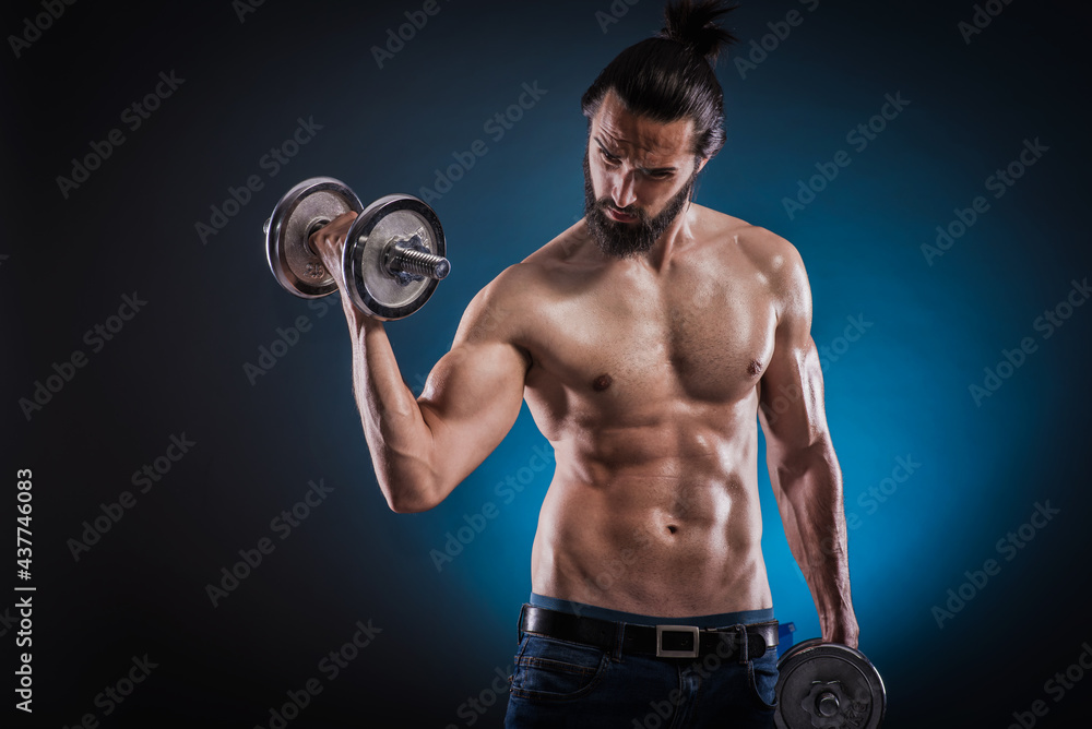 Powerful muscular man lifting weights. Beautiful masculine bearded young hipster man holding dumbbells.