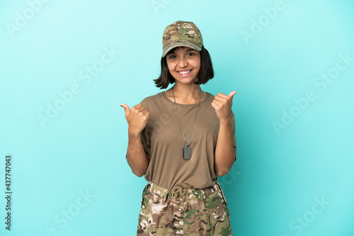 Military mixed race woman with dog tag isolated on blue background with thumbs up gesture and smiling