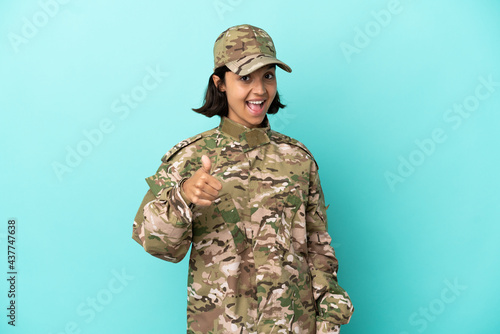 Military mixed race woman isolated on blue background with thumbs up because something good has happened