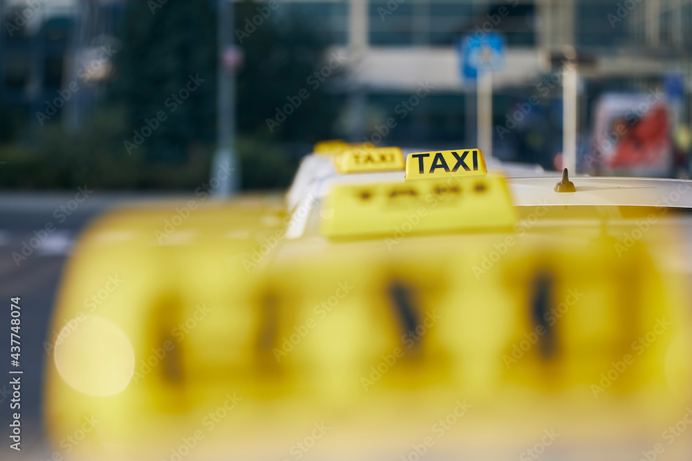 Selective focus on taxi sign on roof.  Car waiting for passenger in city street.