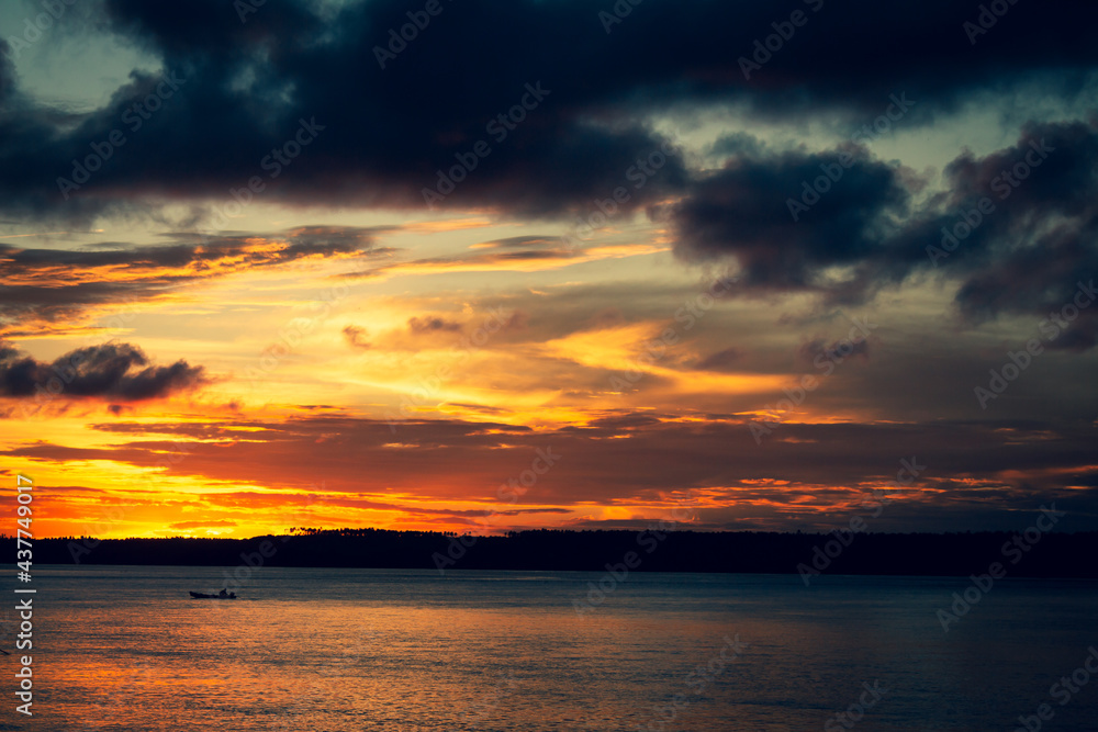 Fine art photography of a vibrantly colored sunset on the lagoon. Small silhouette of a boat.