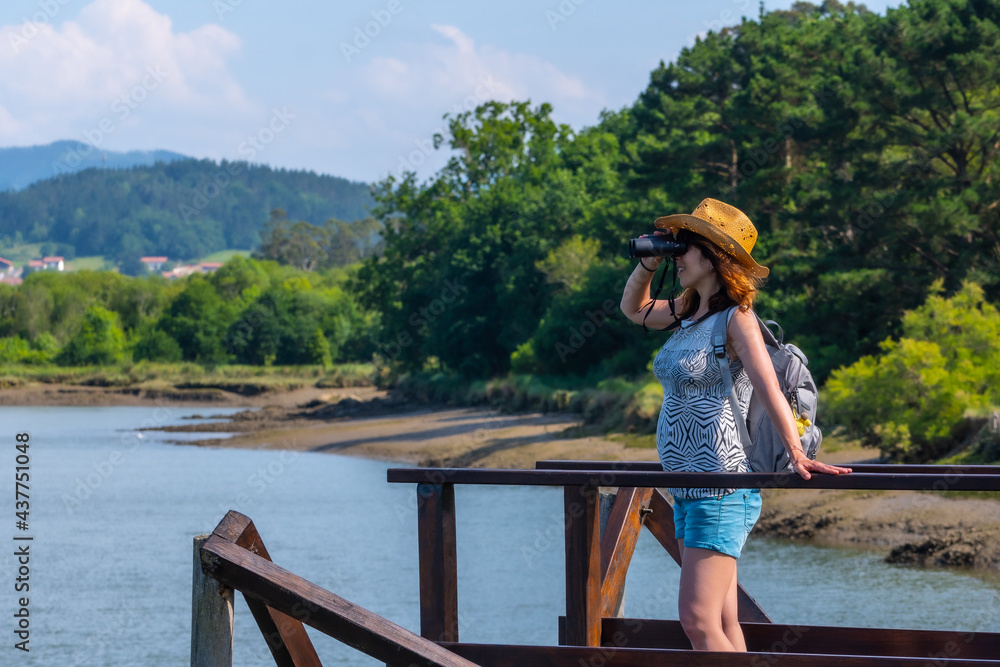 A young woman looking at the birds from the wooden piers of the Urdaibai marshes, a biosphere reserve in Bizkaia next to Mundaka. Basque Country