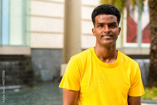 Portrait of handsome black African man wearing yellow t-shirt outdoors in city during summer while smiling