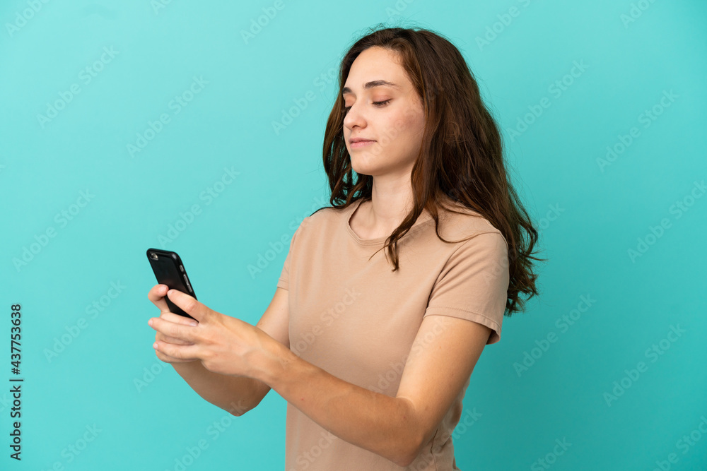 Young caucasian woman isolated on blue background sending a message or email with the mobile Young caucasian woman isolated on blue background sending a message or email with the mobile