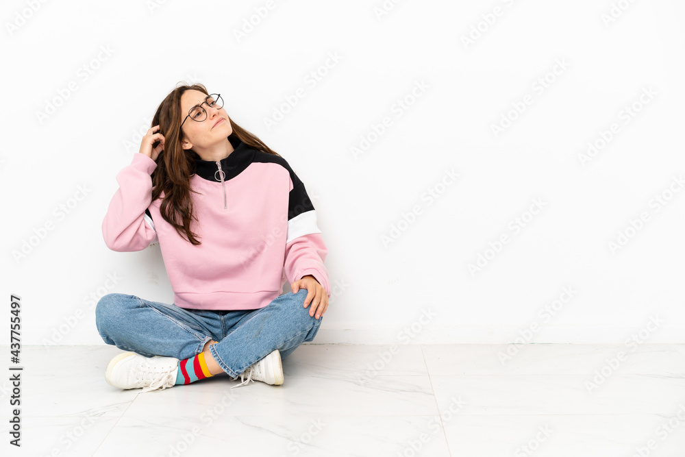 Young caucasian woman sitting on the floor isolated on white background having doubts and with confuse face expression Young caucasian woman sitting on the floor isolated on white background having doubts and with confuse face expression