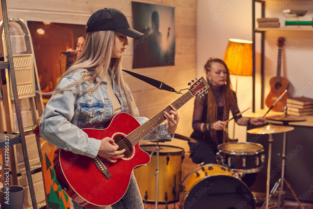 Fototapeta premium Female musicians playing guitar and drum in modern studio
