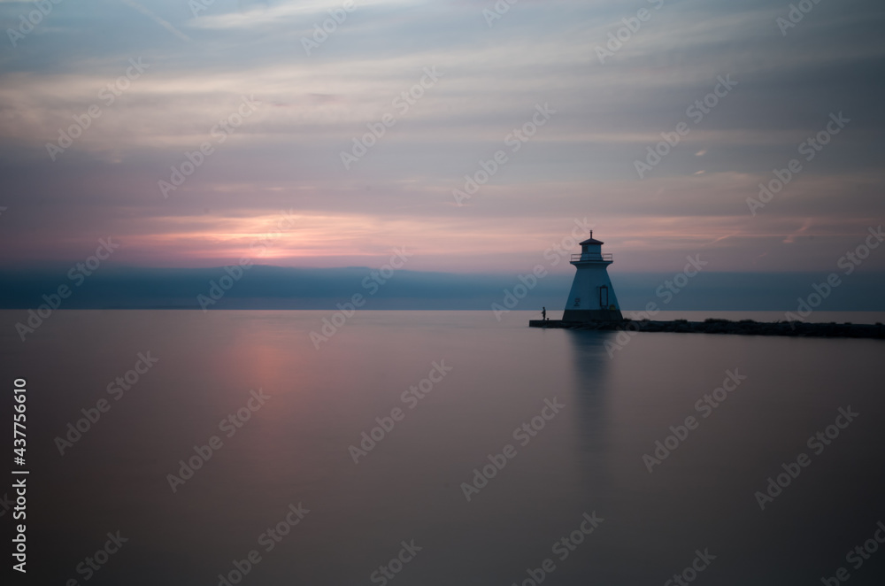 Simple and clean landscape shot of the ocean horizon and and a lighthouse during a beautiful orange/red sunset in Port Elgin, Ontario, Canada.