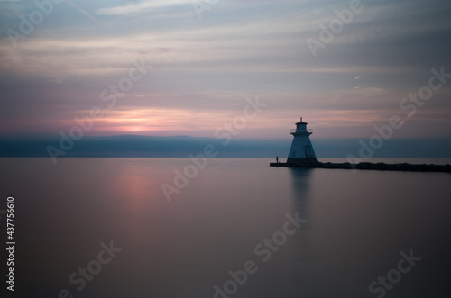 Simple and clean landscape shot of the ocean horizon and and a lighthouse during a beautiful orange/red sunset in Port Elgin, Ontario, Canada. © Asad Soomro