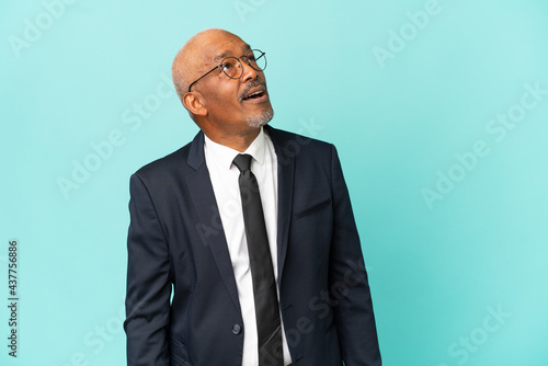 Business senior man isolated on blue background looking up and with surprised expression