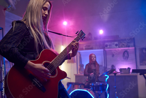 Pretty blond female playing electric guitar during stage performance