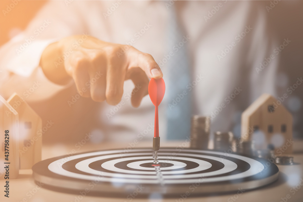 Targeting the business concept, Businessman touch red arrow dart to virtual target dart board,Executive marketing, investment goal and target for business investment concept, mini home and Coins stack Targeting the business concept, Businessman touch red arrow dart to virtual target dart board,Executive marketing, investment goal and target for business investment concept, mini home and Coins stack