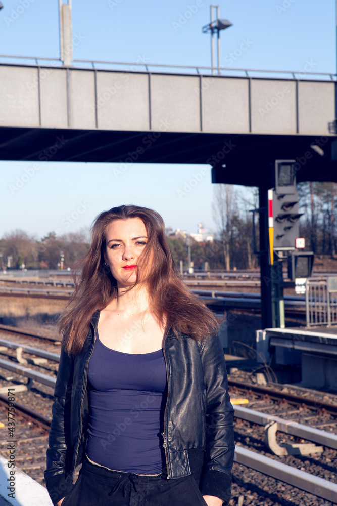 young brunette woman in leather jacket waiting on platform at train station