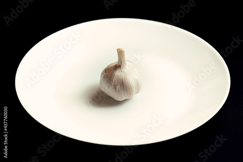 A head of garlic on a white plate on a rough background