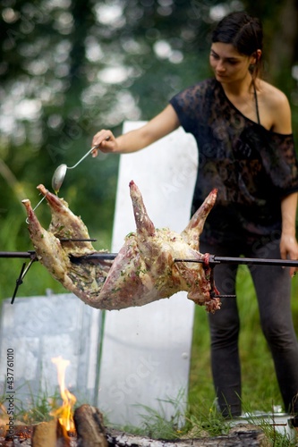 Jeune femme arrose avec sauce marinade méchoui barbecue viande - cuisson nourriture jardin feu à la broche